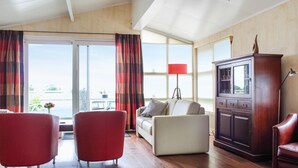 A spacious living room with a sofa, two armchairs, a wooden cabinet, and a large window with curtains.