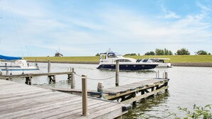 A dock with a boat moored at the pier, a grassy field, and a windmill in the background.