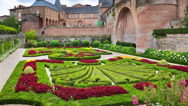 Un bâtiment historique doté d’un jardin à la française, caractérisé par des haies géométriques et une grande variété de fleurs.