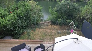Une terrasse en bois, aménagée avec du mobilier d’extérieur, notamment des canapés et une table, qui offre une vue sur une étendue d’eau et une végétation luxuriante.