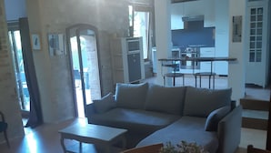 Un salon avec un canapé, une table basse et une table à manger avec des chaises. On aperçoit une cuisine au fond.