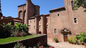 Un bâtiment historique doté d’une tour centrale, de fenêtres en arc de cercle et d’une cour intérieure agrémentée de plantes en pot.