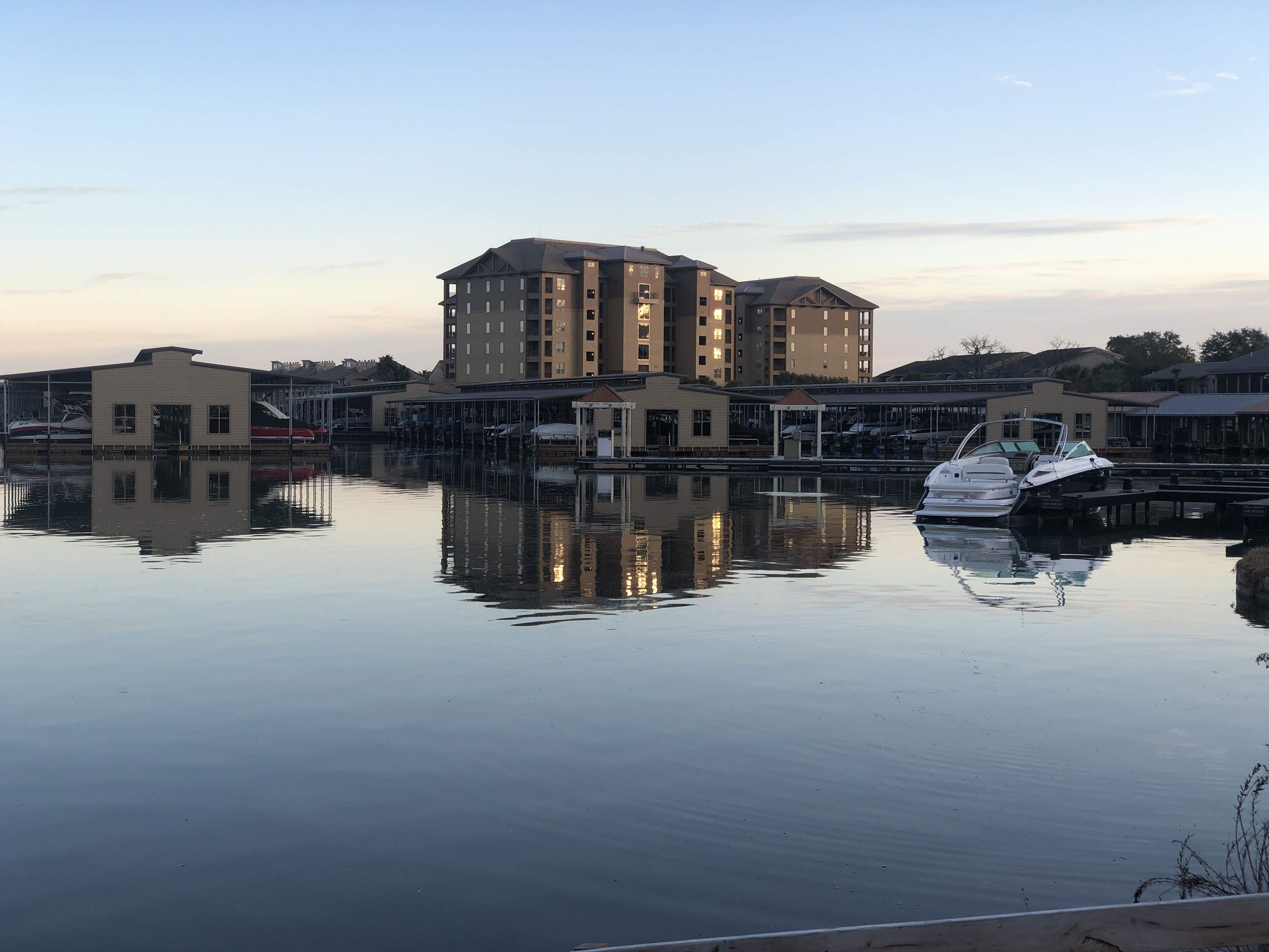 A waterfront property with a large building, a dock with boats, and calm water reflecting the structure.