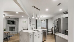 Une cuisine moderne dotée d’un îlot en marbre, d’appareils électroménagers en acier inoxydable, de luminaires suspendus et d’une cheminée.