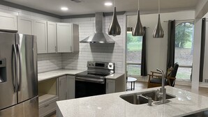 Une cuisine moderne dotée d’appareils électroménagers en acier inoxydable, d’un plan de travail en granit et de luminaires suspendus.
