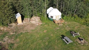 A yurt with a covered entrance, a small wooden structure, and a fire pit area. - Escape to Nature: Cozy Yurt on a Heritage Farm with Trails, Pond, & Sauna (Powassan)