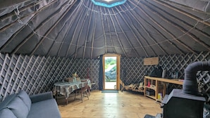 A yurt interior with a wooden floor, a dining table with chairs, a sofa, and a small table with items. - Escape to Nature: Cozy Yurt on a Heritage Farm with Trails, Pond, & Sauna (Powassan)