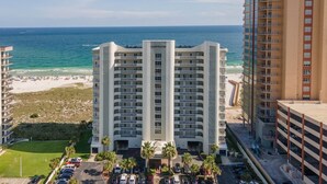 Un hotel de gran altura con vista al mar, varios balcones y un estacionamiento con automóviles.