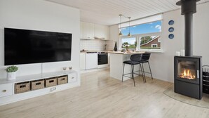 A modern kitchen with a large TV, a built-in stove, and a dining area with bar stools. - 3 bedroom beach front home in Hejls (Hejls)
