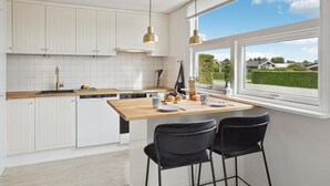 A modern kitchen with white cabinetry, a wooden countertop, and a large window offering a view of the outdoors. - 3 bedroom beach front home in Hejls (Hejls)