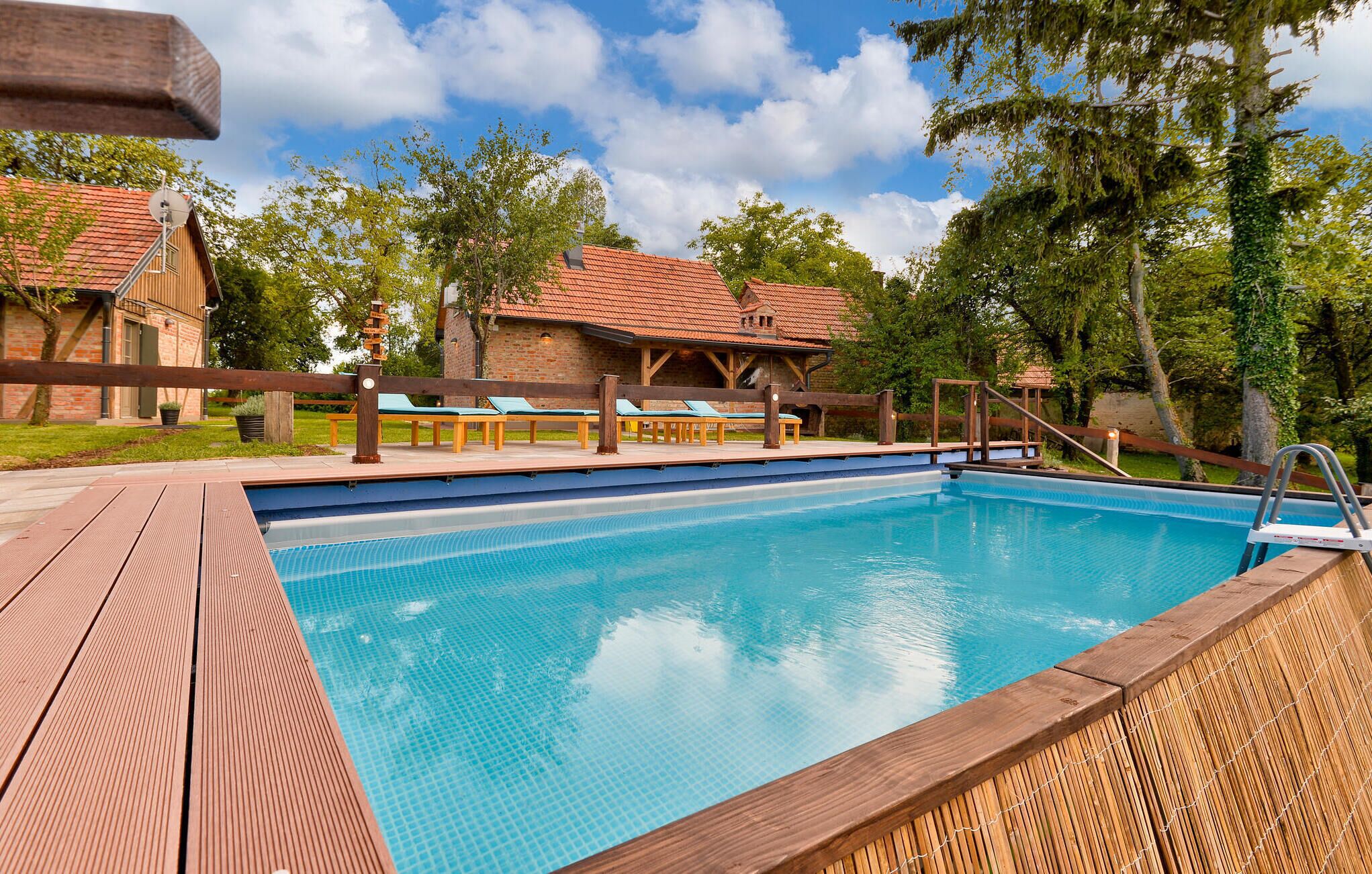 Ein Schwimmbecken mit Holzterrasse, Liegestühlen und einem Holzzaun.