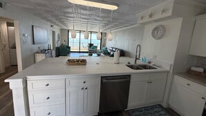 A modern kitchen with a central island, built-in dishwasher, and a view to the living area. - Beautiful Views Just Steps to the gulf! (Fort Myers)