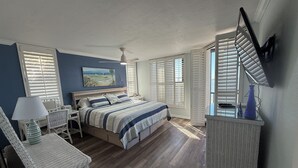 A bedroom with a bed, a desk, wicker furniture, and a painting on the wall. - Beautiful Views Just Steps to the gulf! (Fort Myers)