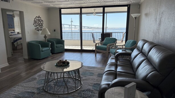 A spacious living room with a large window, a leather sofa, teal armchairs, and a round coffee table. - Beautiful Views Just Steps to the gulf! (Fort Myers)