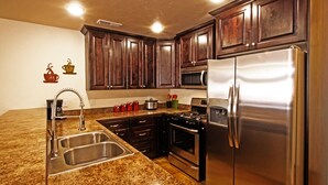 A kitchen with granite countertops, stainless steel appliances, dark wooden cabinets, and a microwave above the stove. - Beautiful Townhome adjacent to the Pool and Hotub (Moab)