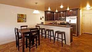 A kitchen with dark wooden cabinets, a stainless steel refrigerator, a microwave, and a dining area with a table and four stools. - Beautiful Townhome adjacent to the Pool and Hotub (Moab)