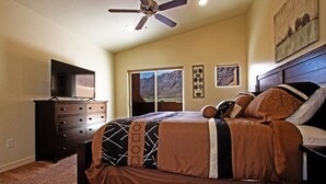 A bedroom with a bed, dresser, ceiling fan, and a view of mountains through the window. - Beautiful Townhome adjacent to the Pool and Hotub (Moab)