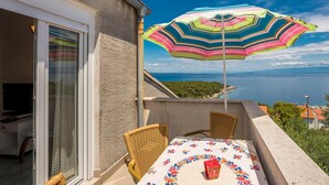 Een balkon met rieten stoelen, een tafel met een tafelkleed met bloemen en een kleurrijke strepen paraplu.
