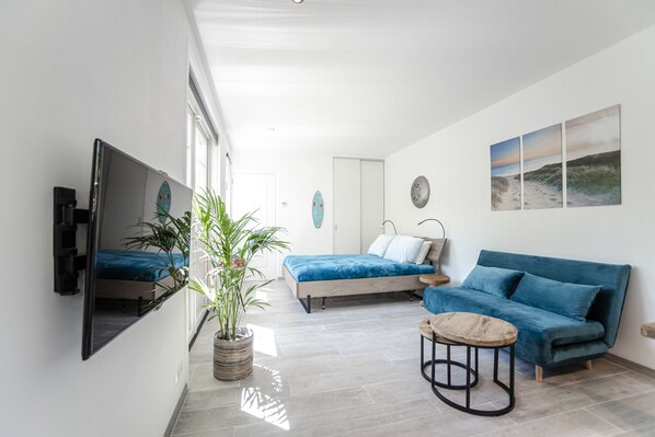 A modern bedroom with a bed, a blue sofa, a small round table, a TV mounted on the wall, and a potted plant.