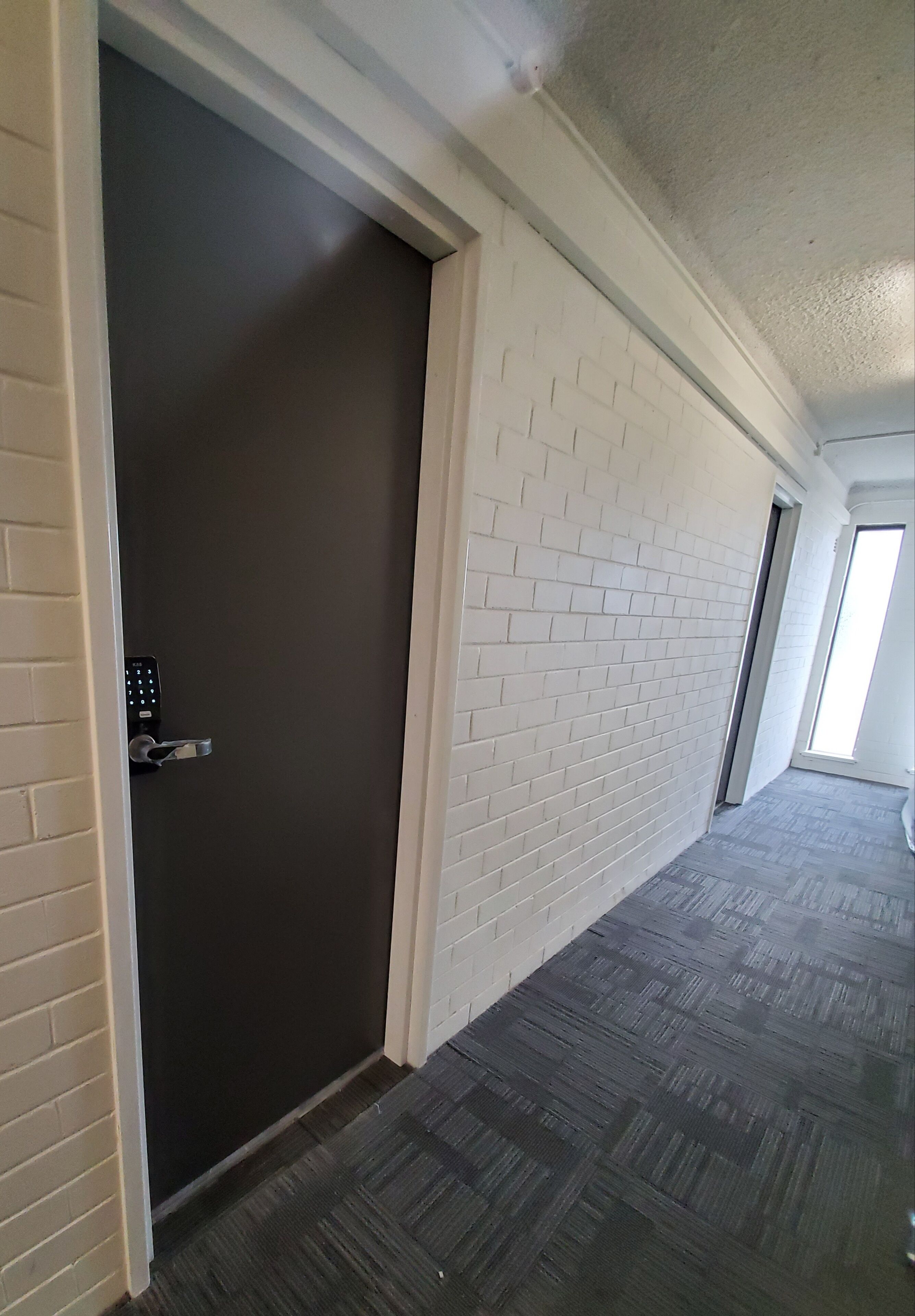 A hallway with a dark door, white brick walls, and a grey floor.
