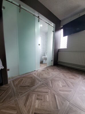 Un baño con suelo en patrón de espiga, inodoro y cabina de ducha con mampara de vidrio.
