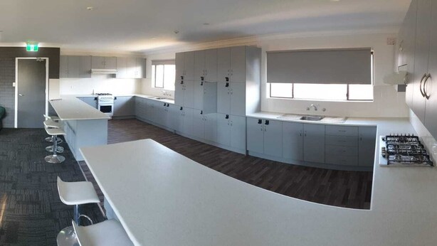 Une cuisine moderne avec des meubles blancs, un îlot central et un coin repas doté de tables et de chaises blanches.