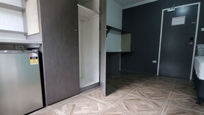Une pièce avec un parquet à motifs en chevrons, un réfrigérateur, une porte et un lit avec un oreiller.