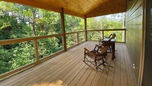 Un muelle de madera con vistas a un bosque. Hay dos mecedoras y una mesa.