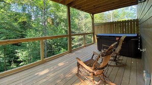 Eine Holzterrasse mit Whirlpool und Schaukelstühlen mit Blick auf einen Wald.