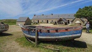 A traditional stone building with a thatched roof, surrounded by a grassy area with a wooden boat. - 2 bedroom awesome home in Plouguerneau (Plouguerneau)