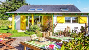 A house with a bright yellow exterior, a small porch with a table and chairs, and a wooden deck with lounge chairs. - 2 bedroom awesome home in Plouguerneau (Plouguerneau)
