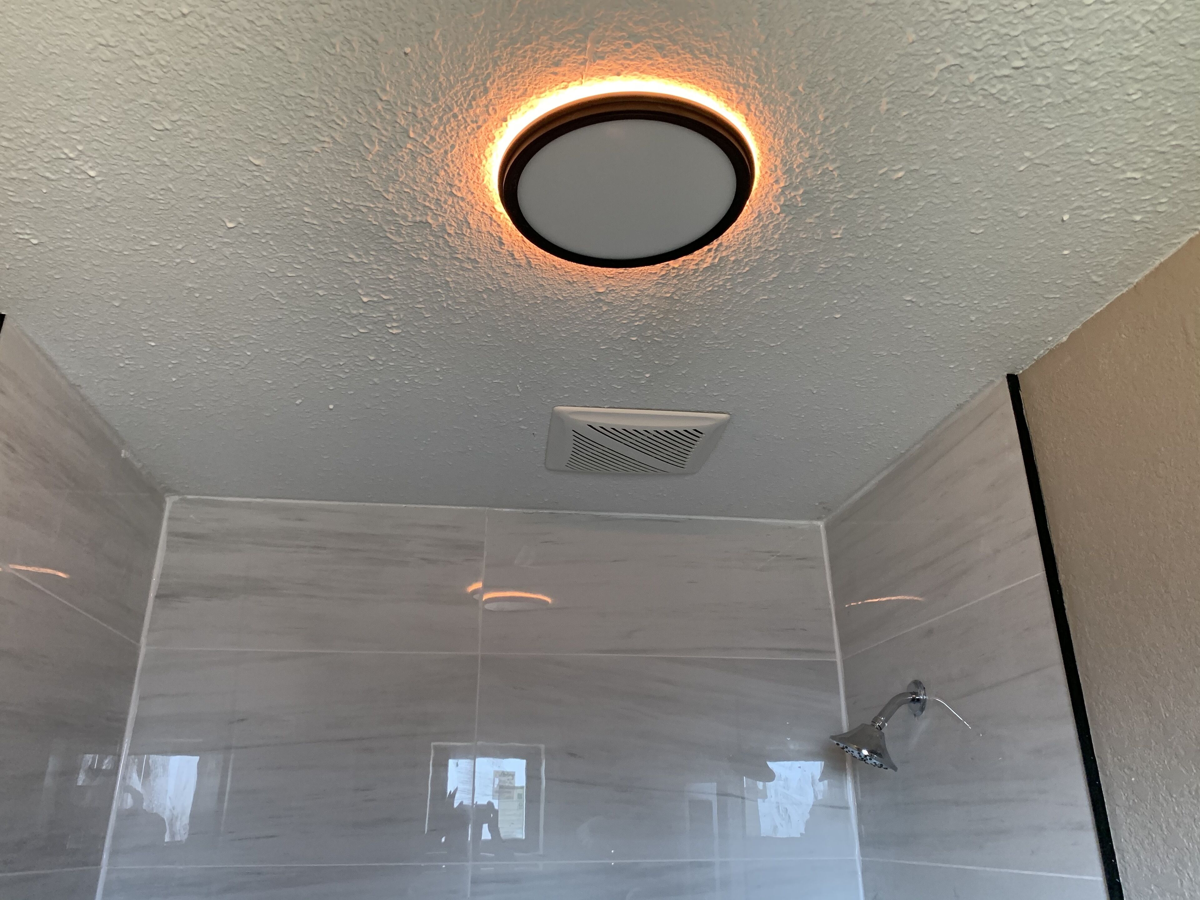 A modern bathroom with a circular light fixture on the ceiling, a showerhead, and a vent.