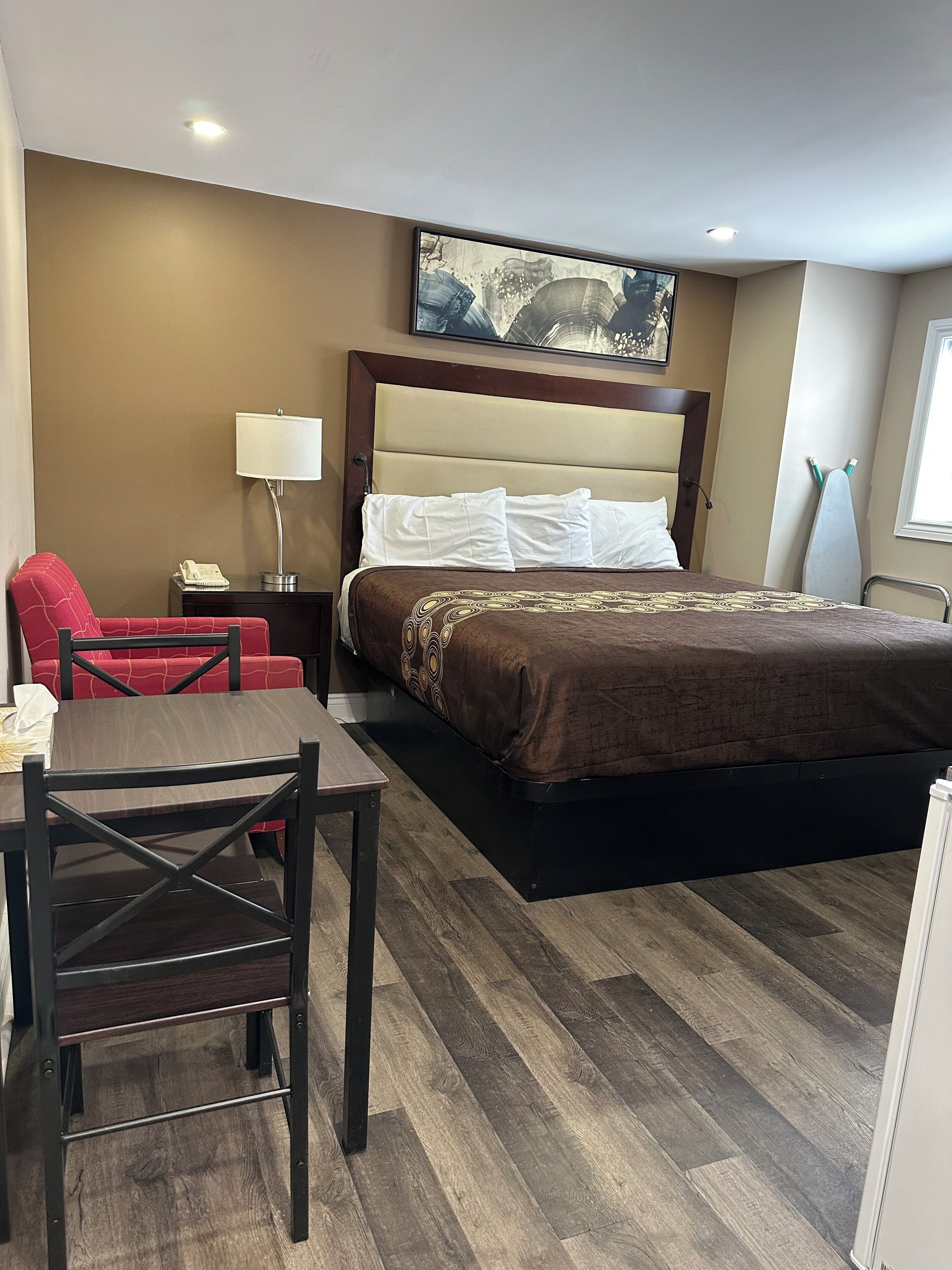 A hotel room with a bed, a desk, a chair, a lamp, and a painting on the wall.