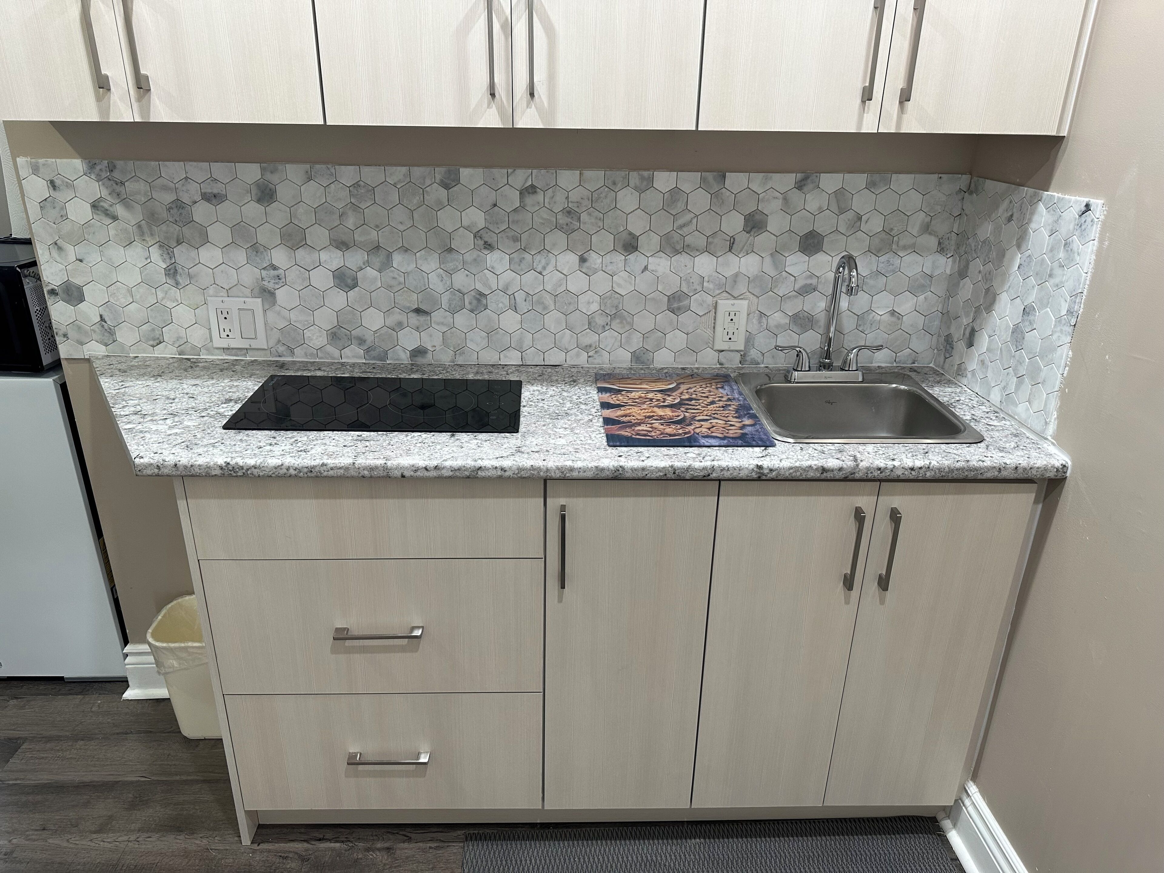 A kitchen with a hexagonal tile backsplash, a double sink, and light-colored cabinets.