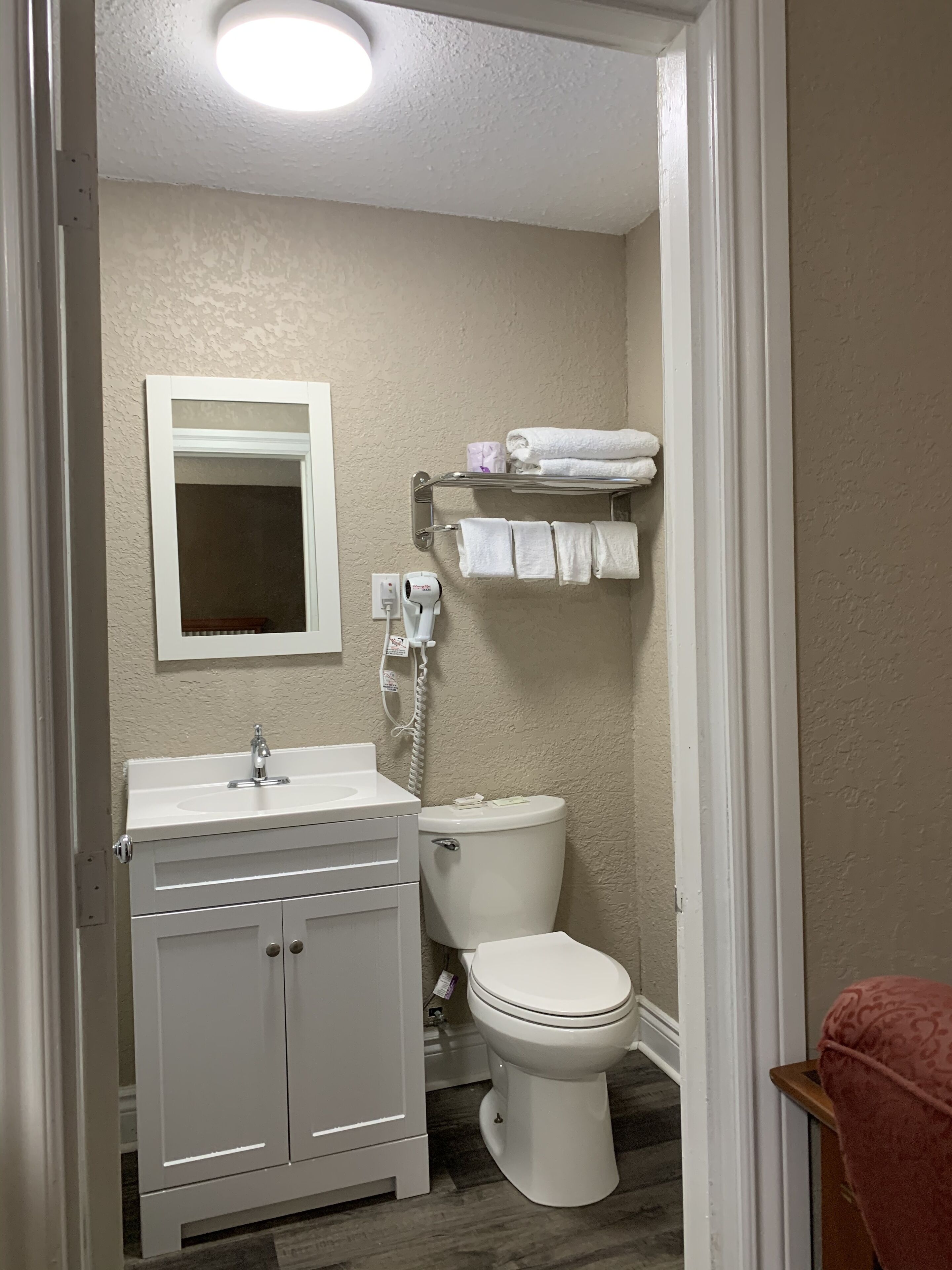 A bathroom with a white sink, mirror, and toilet. There is a towel rack with folded towels and a hairdryer on the wall.
