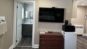 A hotel room with a flat-screen TV mounted on the wall, a wooden dresser, a refrigerator, and a microwave. - Champlain Motor Inn (Pembroke)