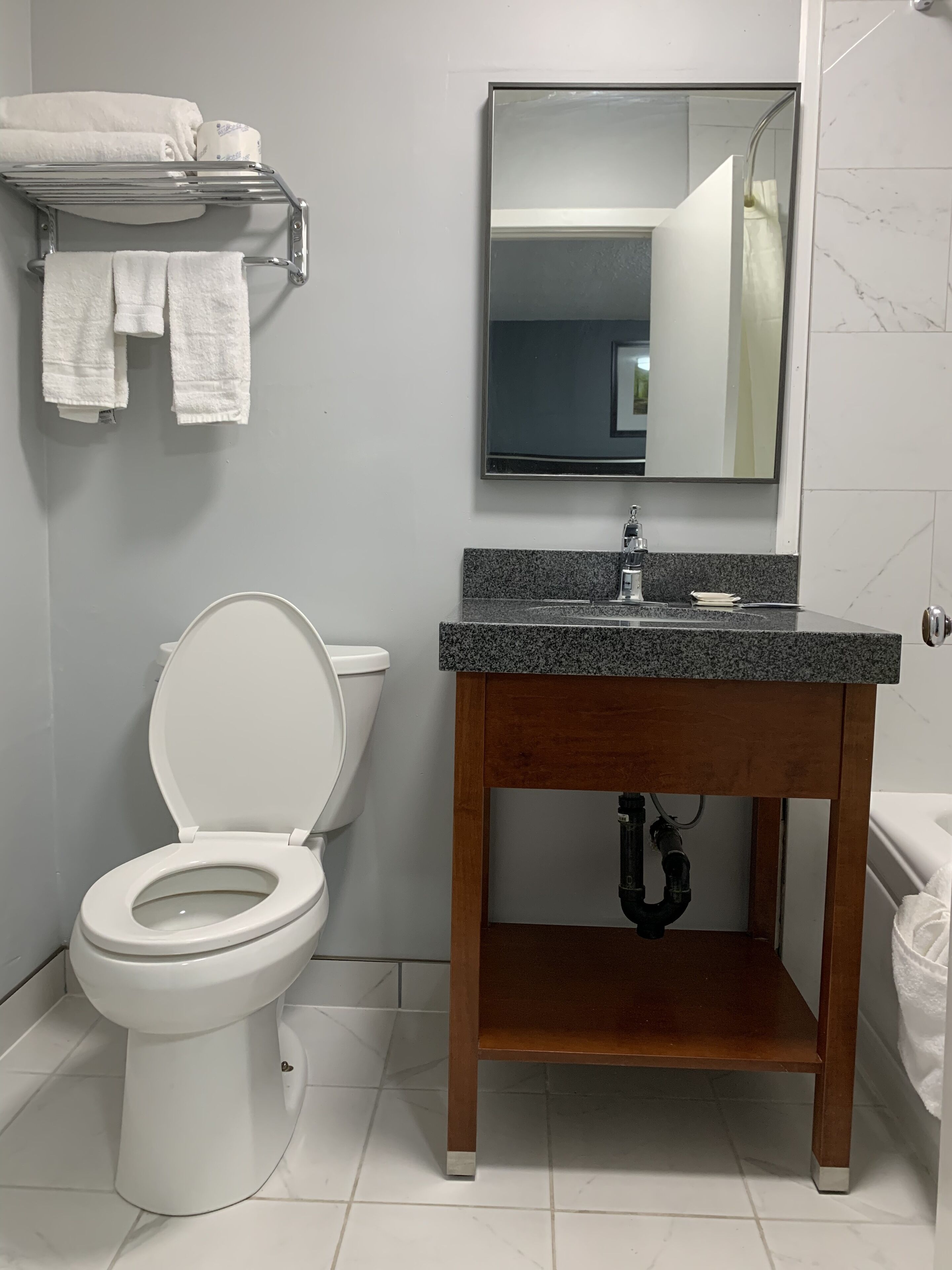 Et badeværelse med et hvidt toilet, en trævask med en granitbordplade, et spejl over vasken og et håndklædestativ med hvide håndklæder.