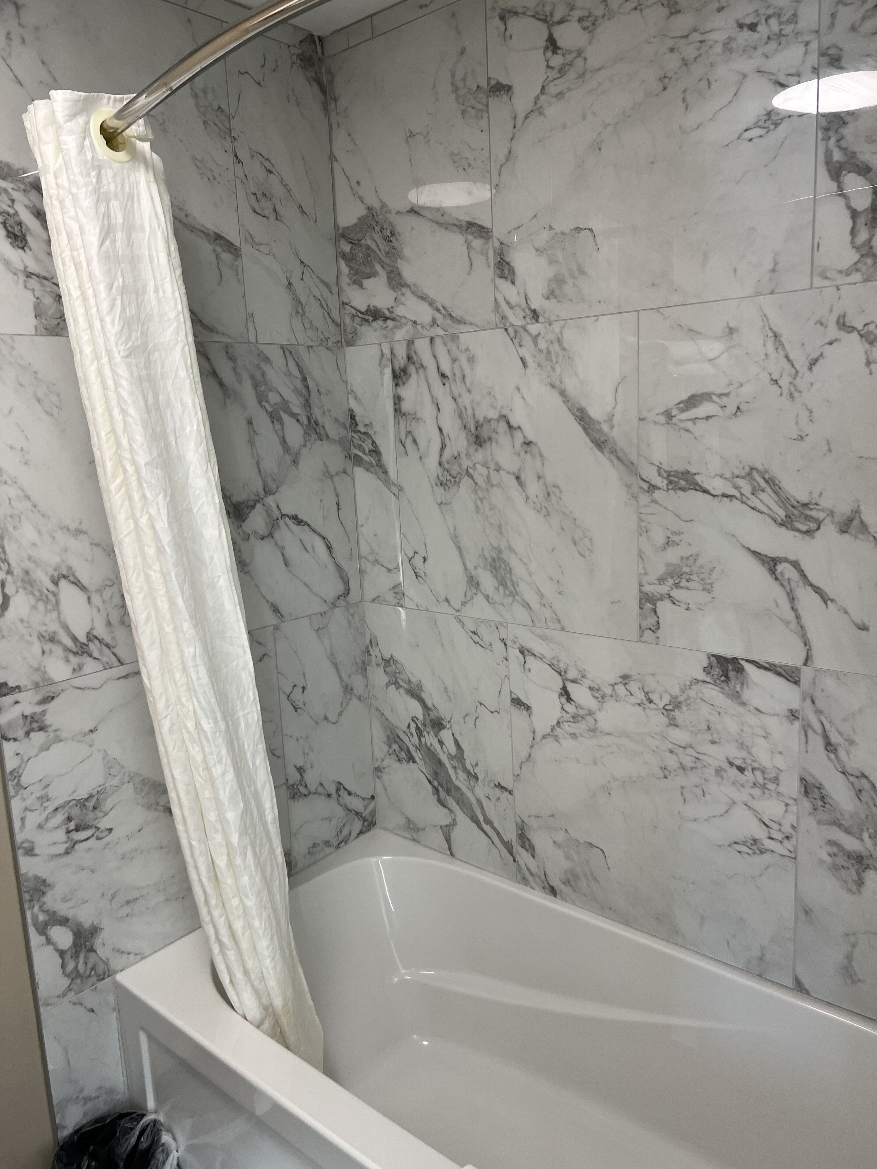A bathroom with a white bathtub, marble walls, and a shower curtain.