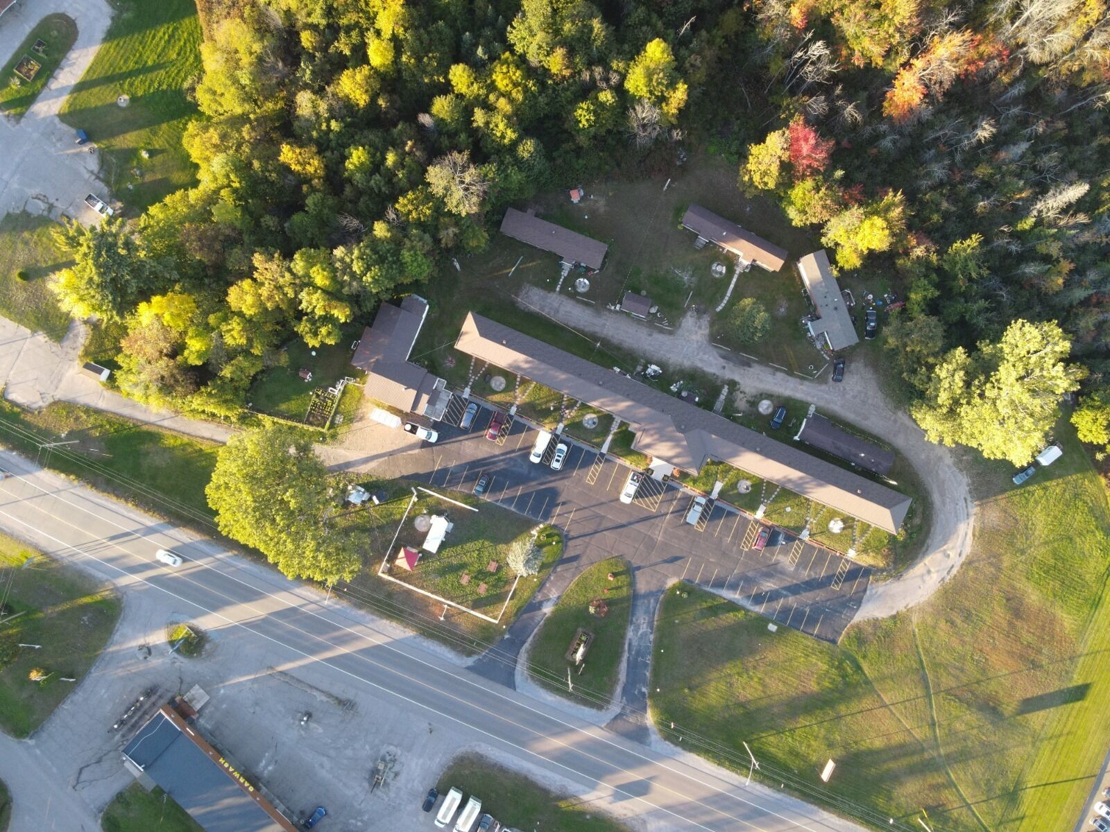 An aerial view of a parking lot with multiple cars, a building with a flat roof, and surrounding greenery.