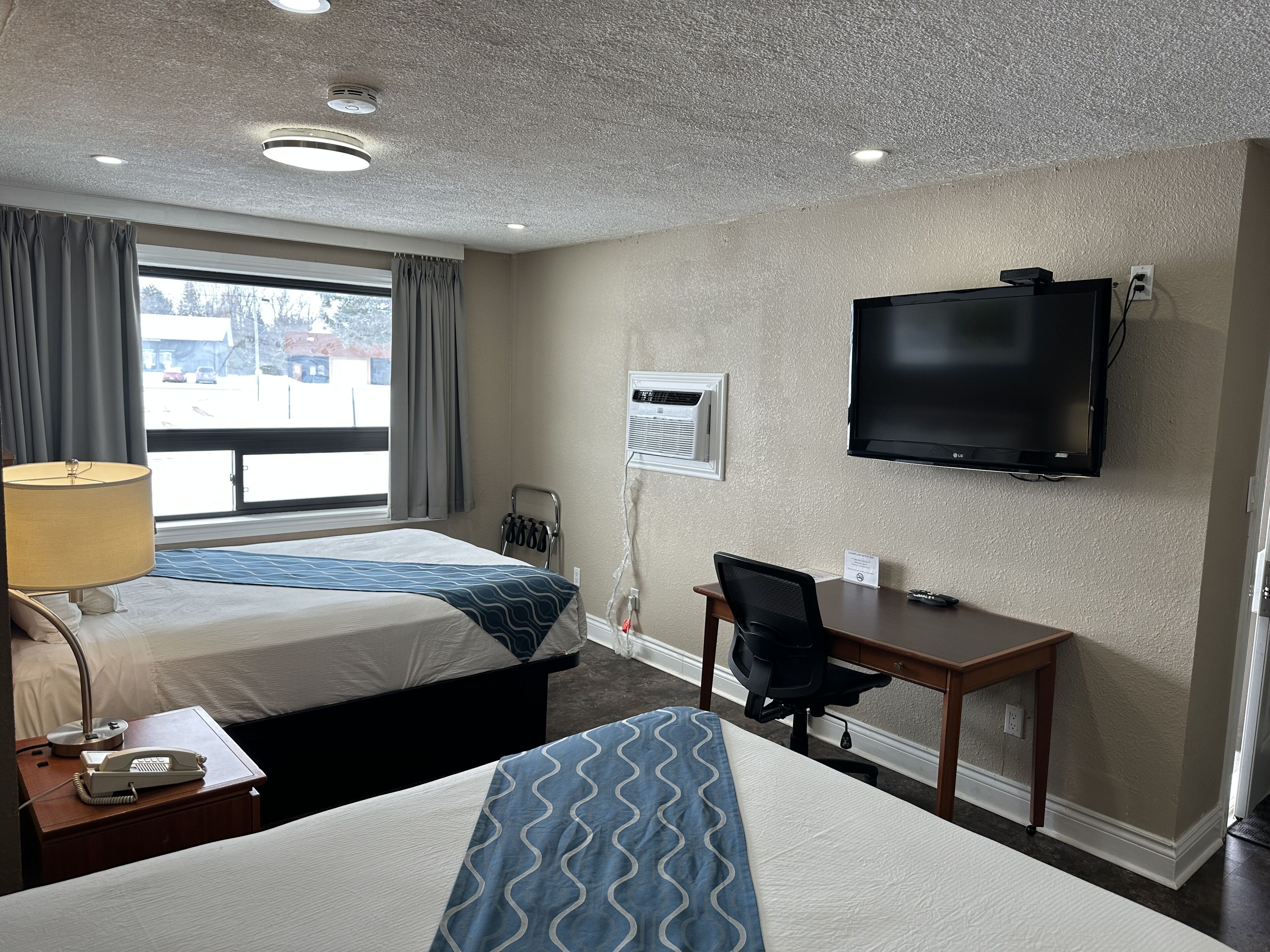 Une chambre d’hôtel avec deux lits, un bureau, une chaise, une télévision et une fenêtre avec des rideaux.