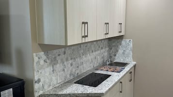 A kitchen with white cabinets, a granite countertop, a hexagonal tile backsplash, a black induction cooktop, a stainless steel sink, and a trash bin.