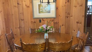 Una sala da pranzo in legno con un tavolo rotondo, sei sedie, un lampadario e un quadro incorniciato appeso al muro.