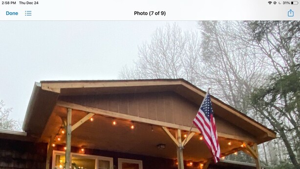 Una baita di legno con un portico decorato con luci e ghirlande, una bandiera americana e vista sugli alberi.
