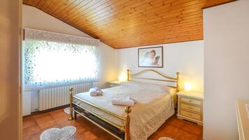 Ein Schlafzimmer mit Holzboden, einem Bett mit goldfarbenem Rahmen, einem Nachttisch mit Lampe und einem Fenster mit Spitzenvorhängen.