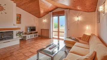Ein geräumiges Wohnzimmer mit Kamin, Fernseher und einem großen Fenster mit Blick ins Freie.