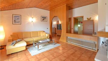 Ein gemütliches Wohnzimmer mit einem gelben Sofa, einem Couchtisch und einem Kamin. Die Decke ist aus Holz und über dem Kamin hängt ein Spiegel.