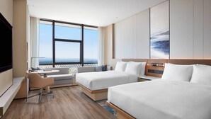 Ein modernes Hotelzimmer mit zwei Betten, einer Couch, einem Schreibtisch und einem großen Fenster mit Blick auf die Stadt.