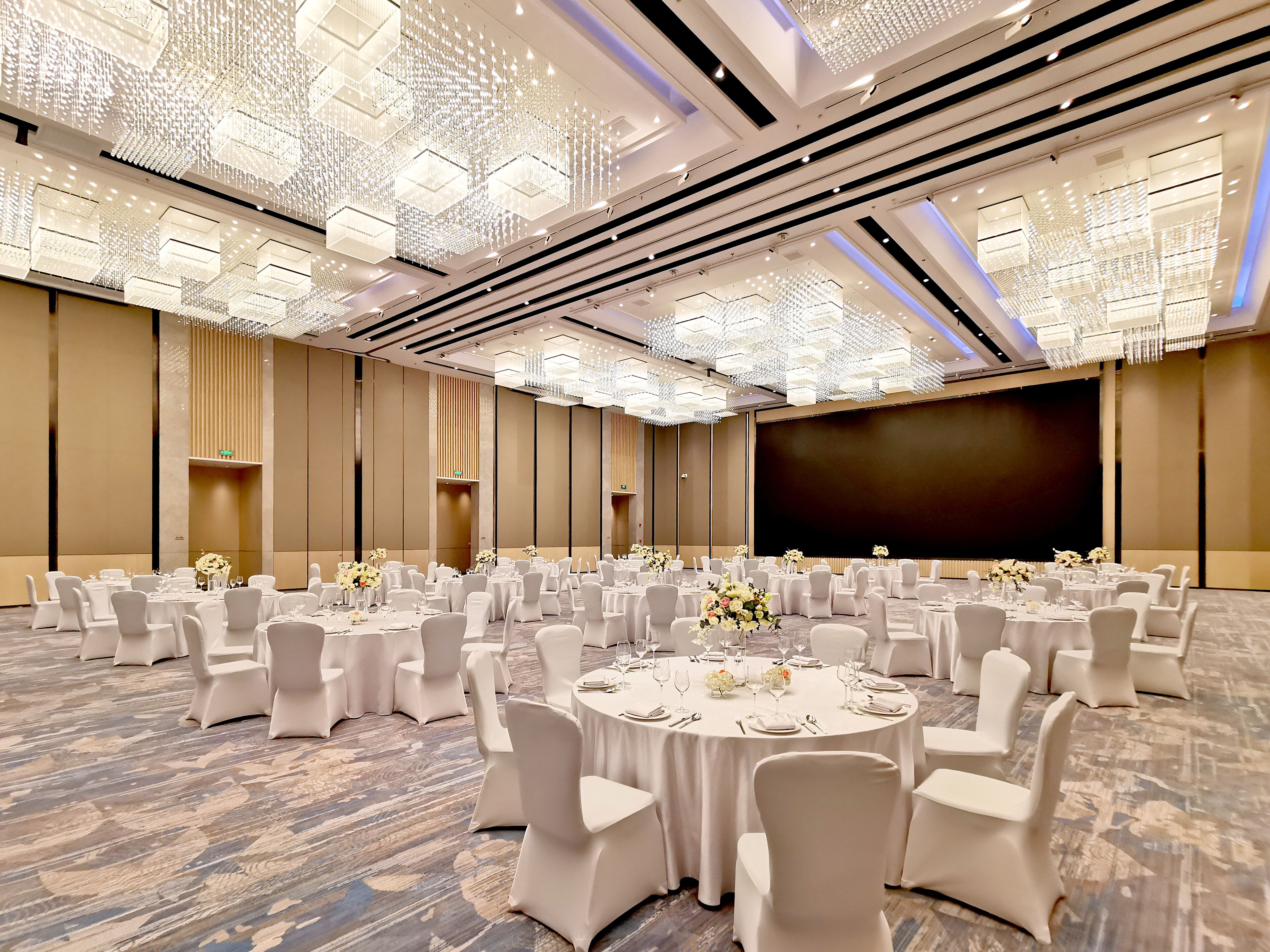 A large conference room with round tables, white chairs, and a large screen.