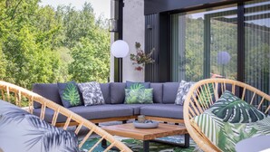 Un área de estar moderna al aire libre con un sofá seccional gris, sillas de mimbre y una mesa de centro de madera.