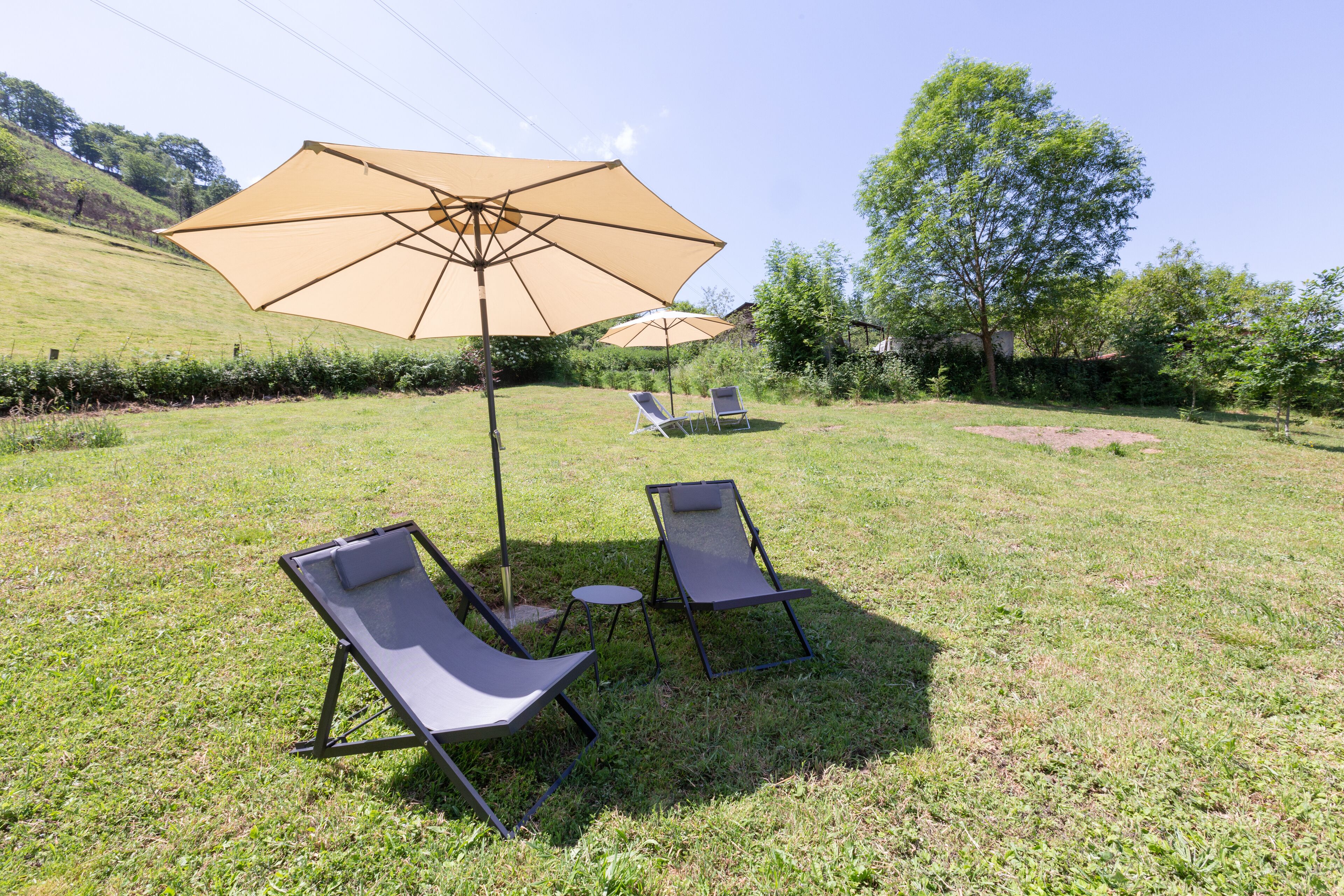 A grassy outdoor area with two lounge chairs and a large umbrella.